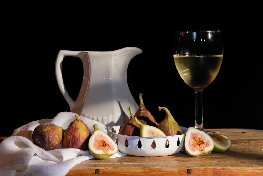 a glass of wine next to a bowl of fruit and a pitcher