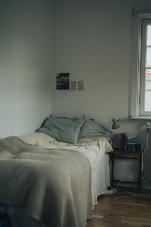 A cozy bedroom corner with soft linens and a minimalist organizer on a nightstand.