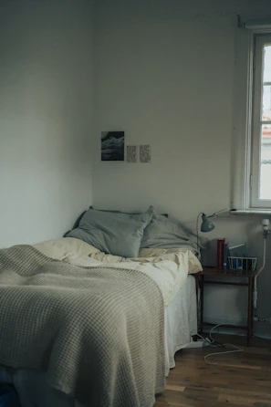 Simple single bed with crisp sheets and a small bedside lamp in a minimalist setting