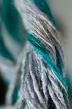 A close-up view of twisted yarn strands, showcasing a combination of gray and teal fibers intertwined.