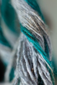 A close-up view of twisted yarn strands, showcasing a combination of gray and teal fibers intertwined.