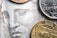 A close-up view of coins placed on a detailed engraving of a face often seen on currency. The coins include various denominations and their metallic surfaces contrast with the intricate line work of the engraved artwork beneath.
