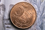 A close-up of a 5 centavos coin from 2019 resting on a banknote with intricate line patterns. The coin features engraved lines, stars, and the denomination.