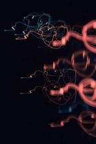 Abstract patterns of blue and red light trails create a dynamic visual effect against a dark background. The light trails intertwine and form intricate loops and curves, conveying a sense of movement and fluidity.