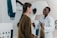 Two women are engaged in conversation in a medical setting, one wearing a white coat, suggesting she is a healthcare professional. The environment contains medical equipment, possibly indicating a check-up or consultation is taking place.