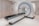 A large, modern medical imaging machine, possibly a CT scanner, is situated in a clean and well-lit medical room. The machine is white with grey accents and features a circular opening with a long table extending from it, which can slide the patient in for scanning. On the side of the scanner, there are control panels with digital displays and buttons.
