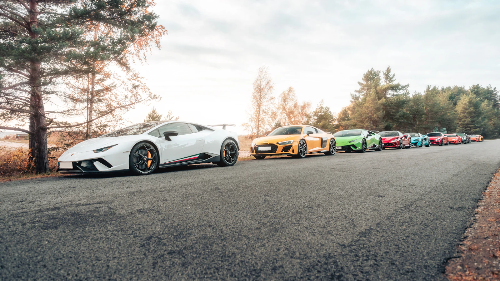 White Lamborghini Huracan at the front of a lineup of supercars on a road
