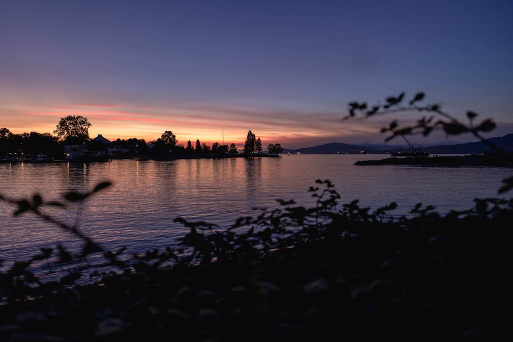 a body of water with trees and a sunset in the background