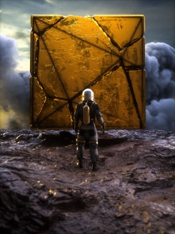 An astronaut in a futuristic suit stands in front of a large, mysterious golden cube with intricate designs. The surrounding landscape appears rugged and extraterrestrial, with dark, rocky terrain under a dramatic, cloudy sky.