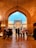 A group of people stand under a large archway, looking towards an intricately designed mosque with domed rooftops and minarets. The scene is vibrant with the warm glow of lights illuminating the mosque against a clear blue sky.