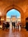 A group of people stand under a large archway, looking towards an intricately designed mosque with domed rooftops and minarets. The scene is vibrant with the warm glow of lights illuminating the mosque against a clear blue sky.