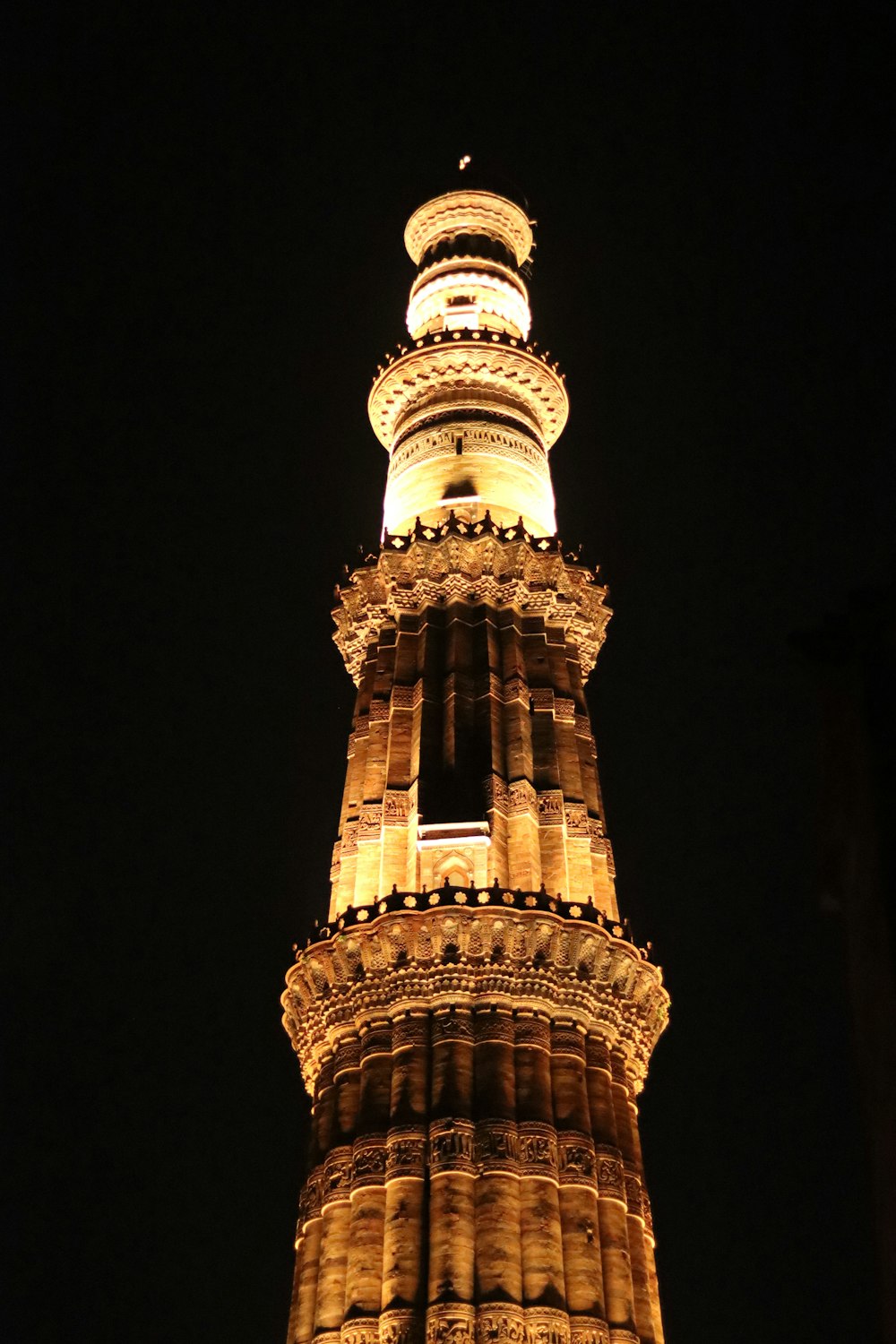 a tall tower with a lit up top with Qutub Minar in the background
