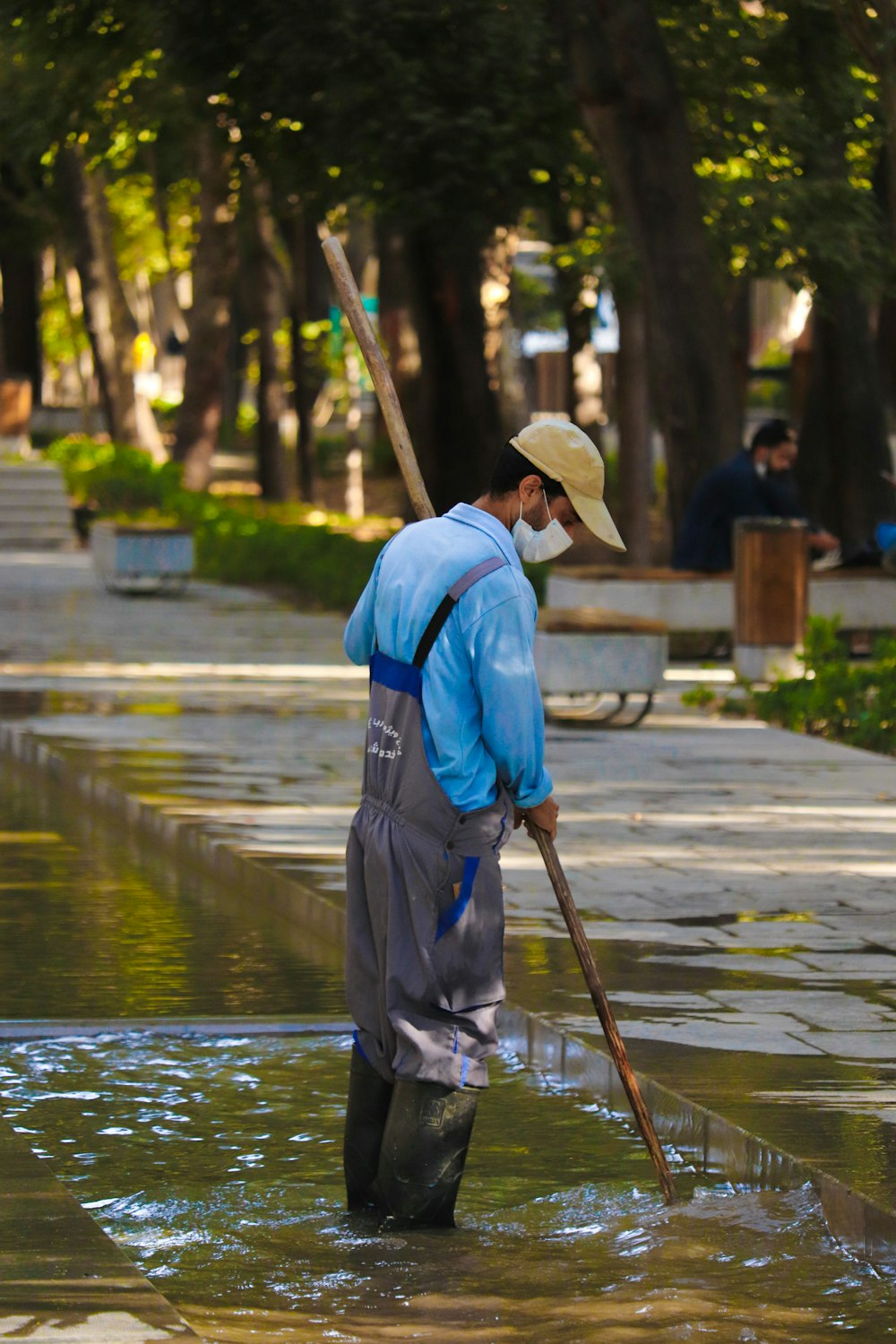 a man in a blue shirt and hat holding a stick in a flooded area