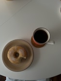 A steaming cup of drip coffee next to a mini donut.