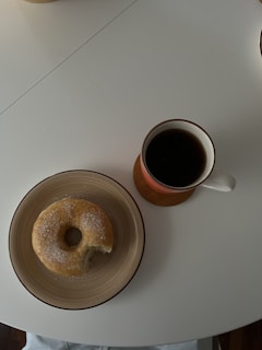 A steaming cup of traditional drip coffee beside a plate of donuts.