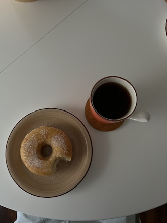 A cozy coffee cup steaming beside a plate of assorted donuts and scones on a wooden table.