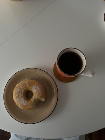 A steaming cup of traditional drip coffee beside a plate of donuts.