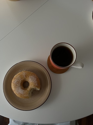 A steaming cup of coffee beside a plate of donuts.
