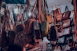 A variety of handbags are hanging in a crowded market stall, each suspended by straps. The bags display different styles, colors, and sizes, creating a vibrant and busy scene. There are people partially visible at the bottom, potentially browsing the collection.