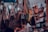 A variety of handbags are hanging in a crowded market stall, each suspended by straps. The bags display different styles, colors, and sizes, creating a vibrant and busy scene. There are people partially visible at the bottom, potentially browsing the collection.