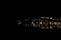 Nighttime cityscape of Dubai with illuminated skyscrapers reflecting on the water.