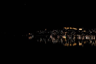 Nighttime cityscape of Dubai with illuminated skyscrapers reflecting on the water.