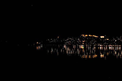 Nighttime cityscape illuminated with colorful lights and reflections on water.