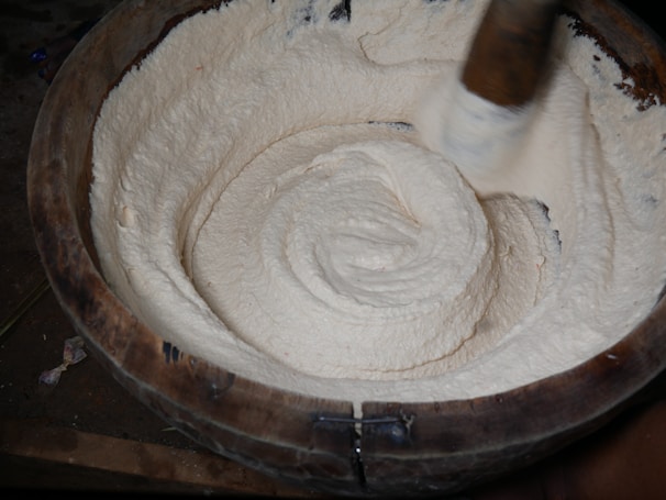 Close-up of a hand stirring fresh ghee in a wooden bowl.