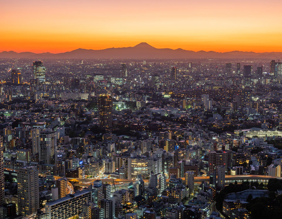 Panoramic view of cityscape at sunset with buildings illuminated against warm orange sky