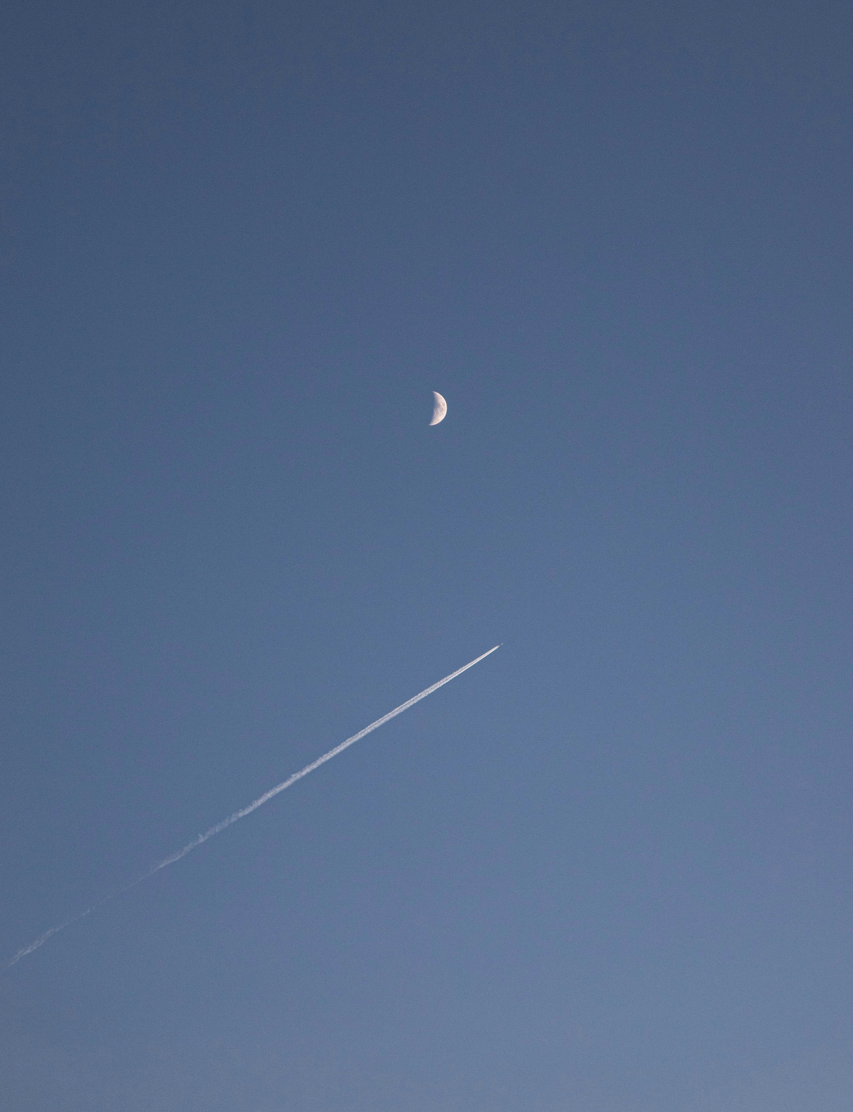 An airplane leaving a diagonal trace just below the moon.