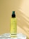 A yellow bottle of hair care product with a green pump sits on a white surface. The background is a smooth, pale yellow surface with soft shadows.