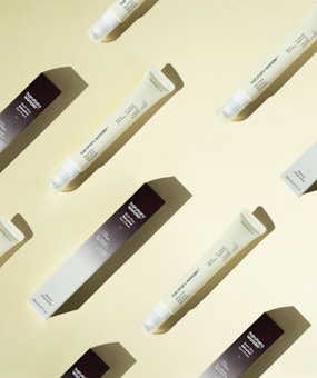 Several tubes of skincare product and their boxes are arranged diagonally on a light yellow background, casting soft shadows. The tubes are labeled with product information.