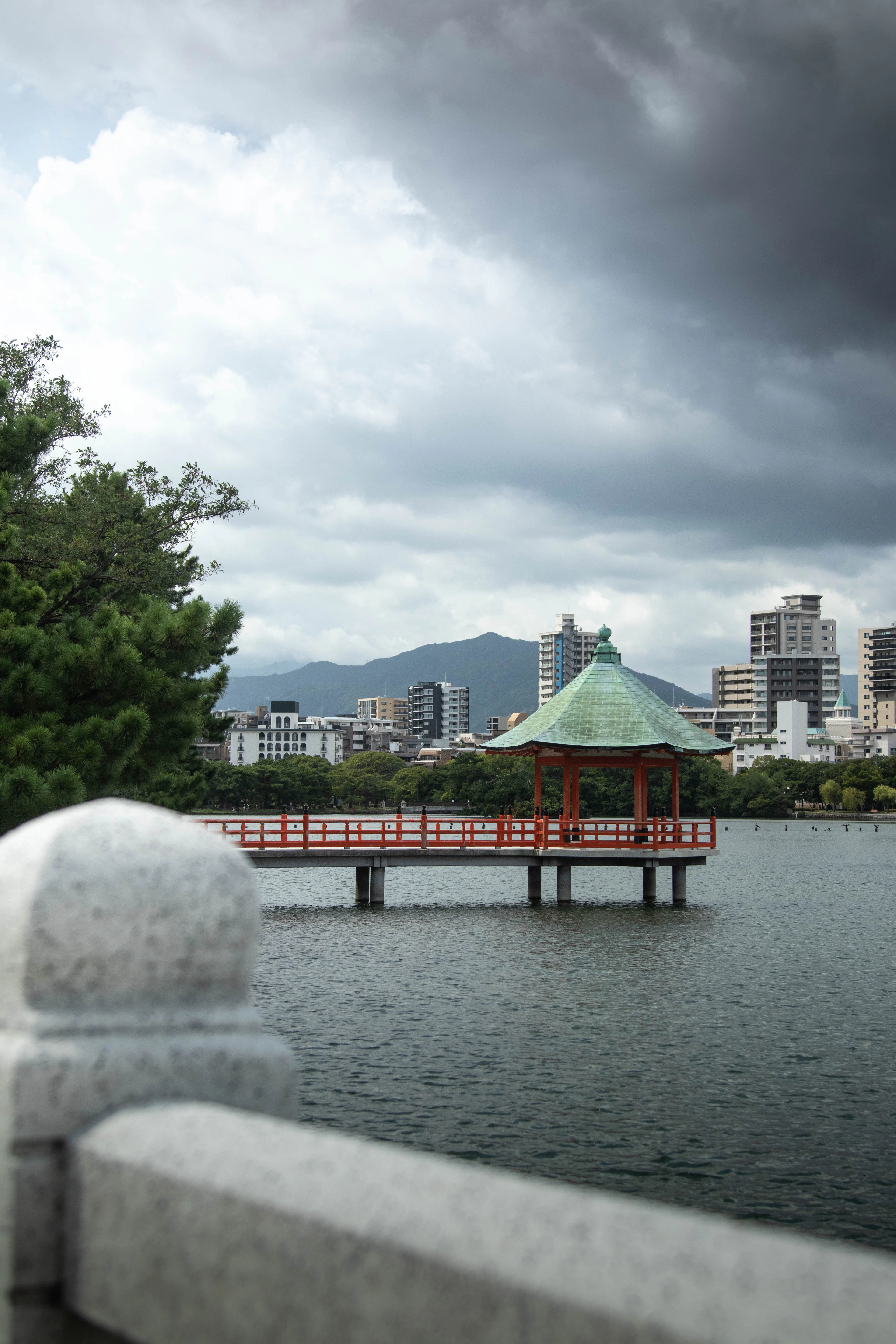 A white swan-shaped pedal boat floats on Ohori Park's lake with Fukuoka's skyline behind it.