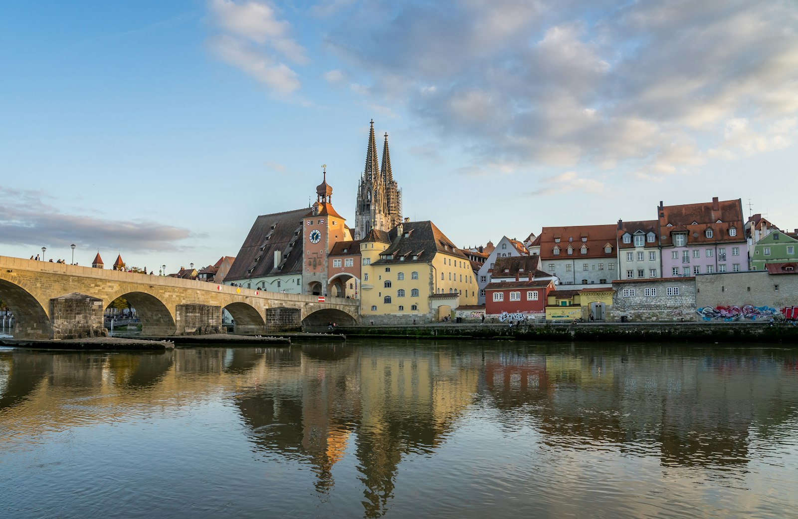 Regensburg's medieval Stone Bridge, bridge tower and cathedral spires reflected in the Danube at golden hour