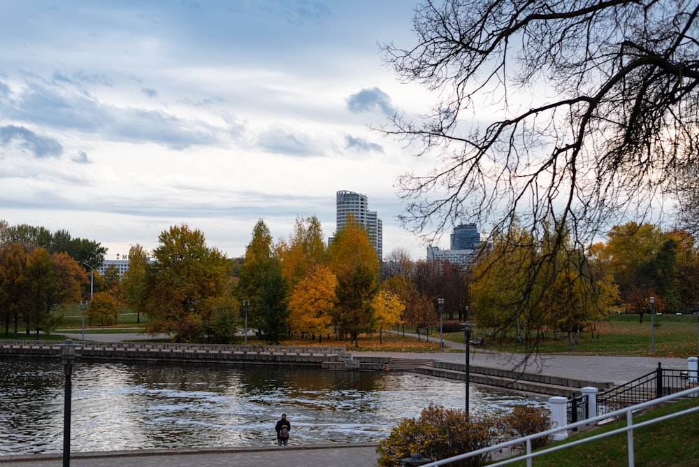 a body of water with trees around it and buildings in the background