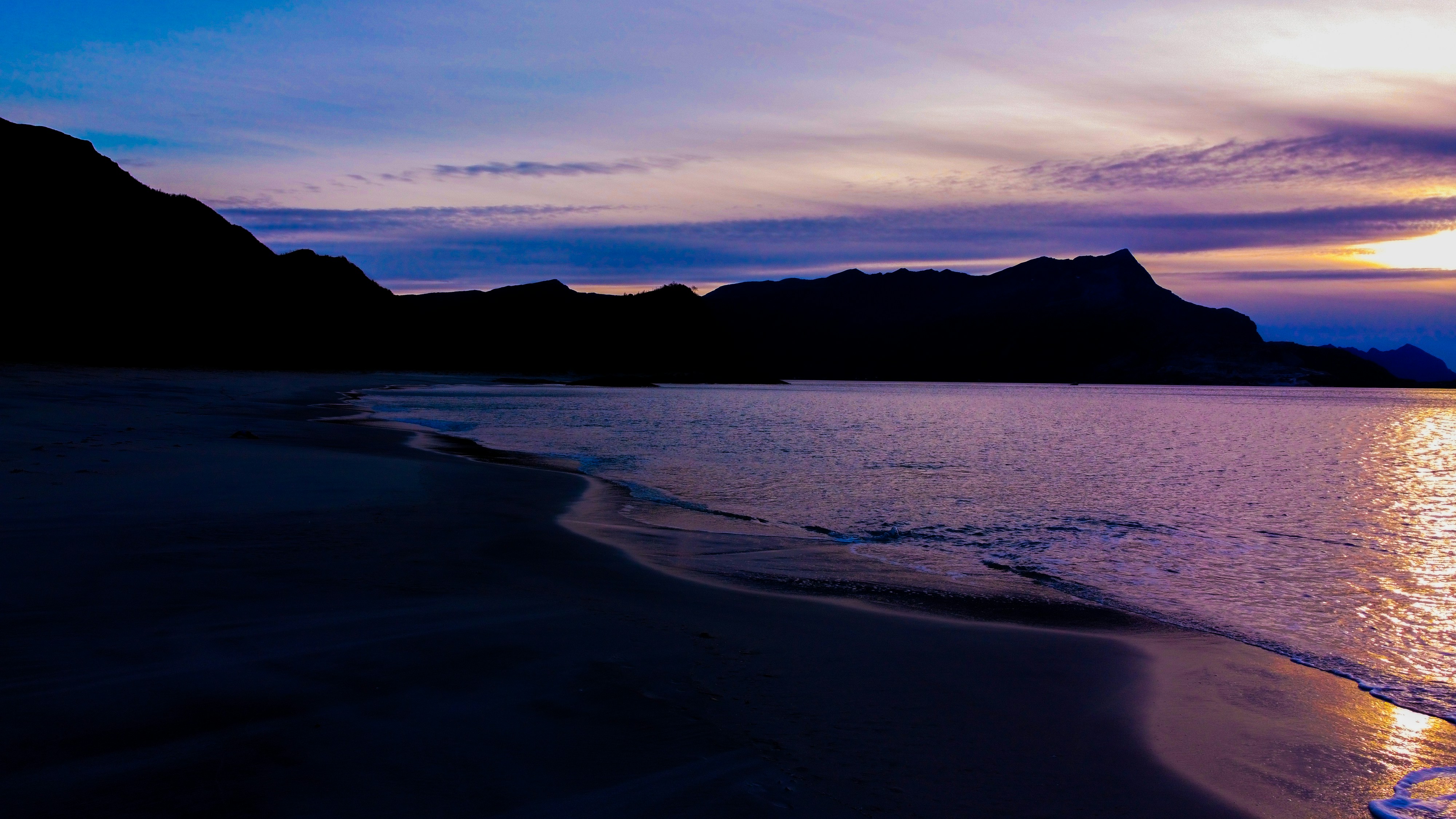 a beach with a body of water and mountains in the background