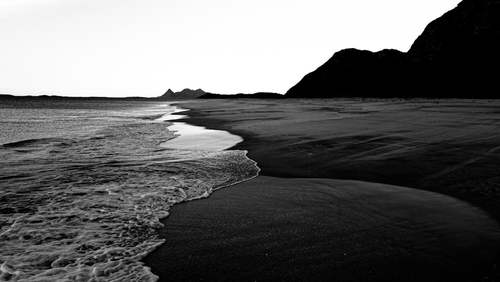 a black and white photo of a beach with waves crashing on it