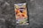 A Pokémon trading card game booster pack titled 'Sword & Shield: Brilliant Stars' is centered on a rough, textured gray surface. The pack features colorful artwork with a prominent orange and yellow dragon-like creature, exuding a dynamic and energetic feel.