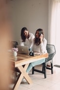 a couple of women sitting at a table with a laptop