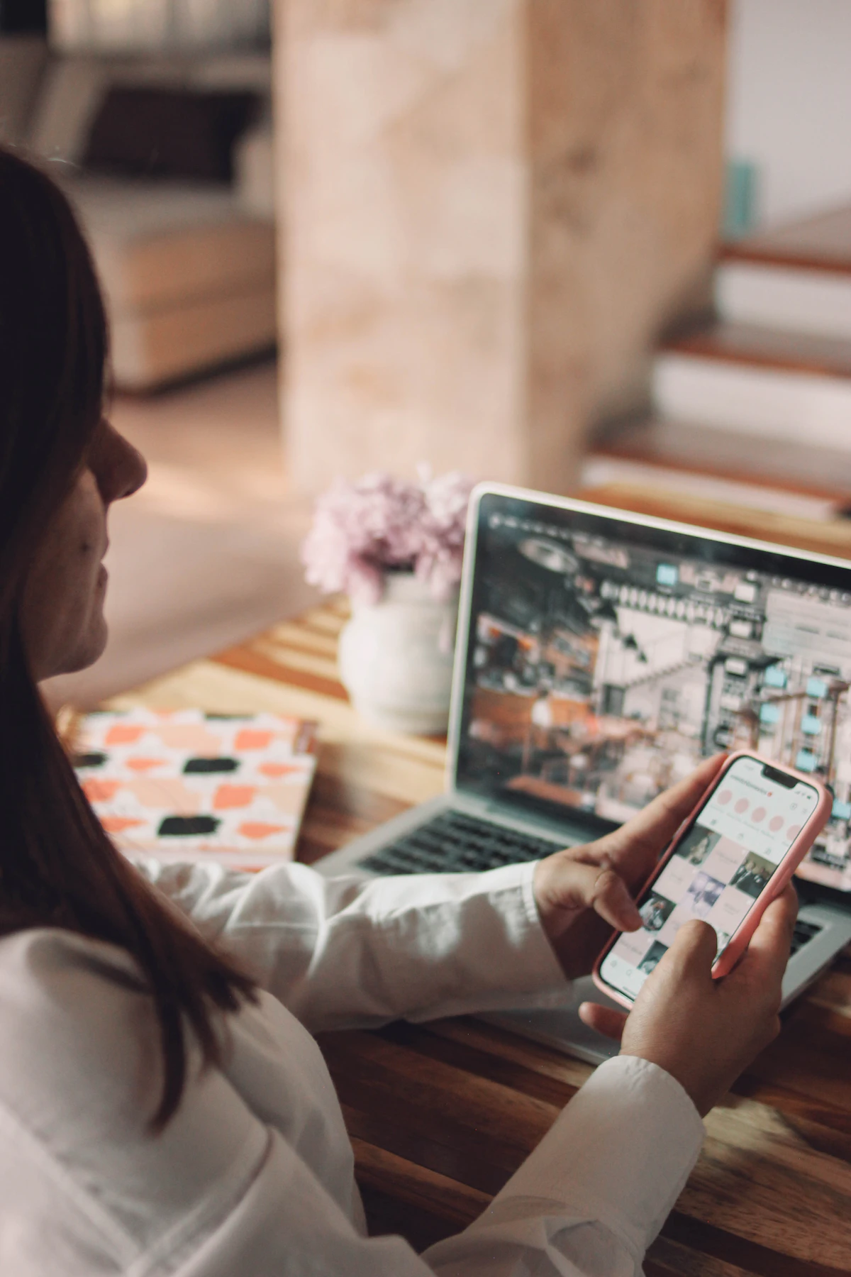 Mujer trabajando con teléfono y laptop en una mesa de madera