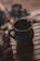 Close-up of a steaming enamel mug resting on a weathered wooden table beside a glowing campfire.