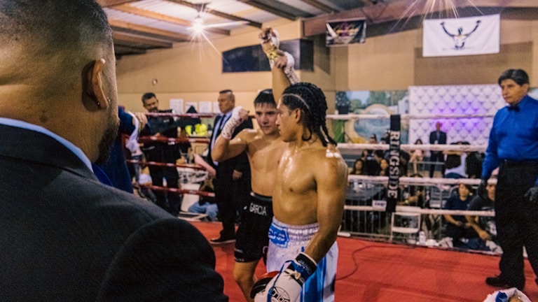 A boxer raising his championship belt high in the ring, celebrating victory.