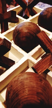 A close-up view of a wooden tic-tac-toe game set with spherical and cross-shaped pieces arranged in a white grid.