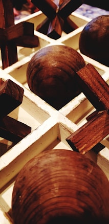 A close-up view of a wooden tic-tac-toe game set with spherical and cross-shaped pieces arranged in a white grid.