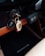 A set of car keys hanging in the ignition of a car, with a leather keychain displaying a Porsche emblem. The dashboard surface is visible, featuring a wooden trim and buttons, creating a vintage or classic car aesthetic.