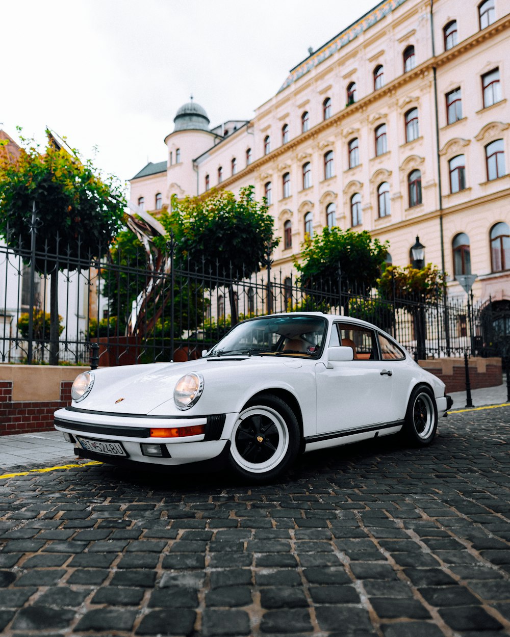 a white car parked on a brick road in front of a building