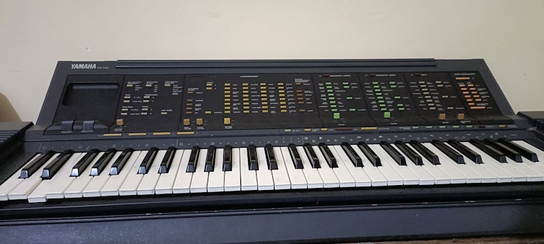 An electronic keyboard with a wide range of control buttons and features. The keys are black and white, typical of a piano, and the upper section contains numerous labels and switches for different sound settings.