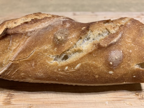 Close-up of golden crust sourdough loaf resting on a rustic wooden board.