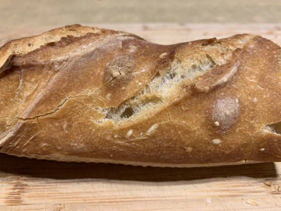 Close-up of a golden crusted sourdough loaf resting on a rustic wooden board.
