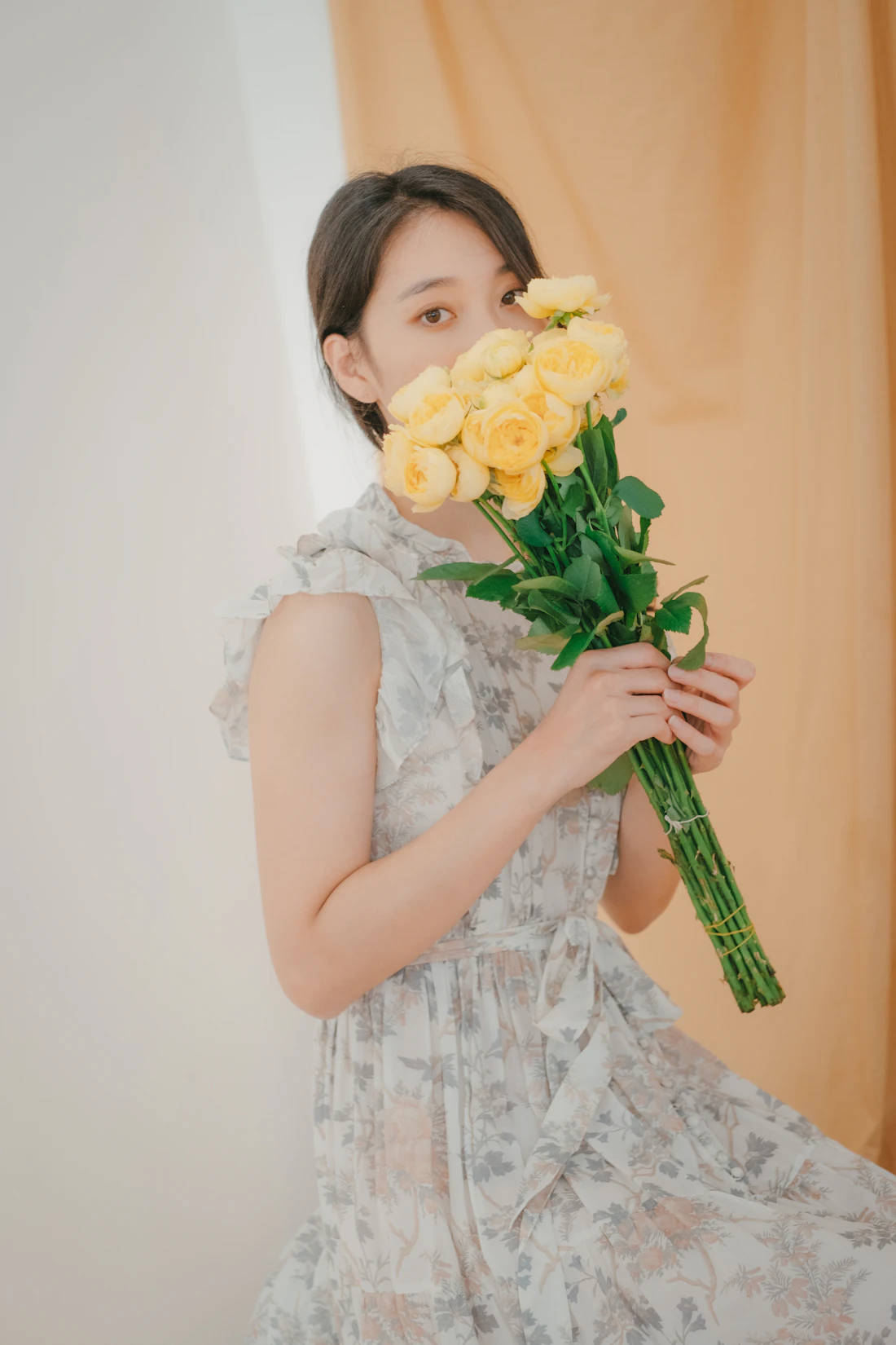 Model in a white eyelet dress holding a bunch of yellow roses